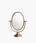 A vintage-style tabletop mirror with an oval shape and bronze finish. It features an adjustable frame resting on a decorative, circular base. | Wildwood Home Co.