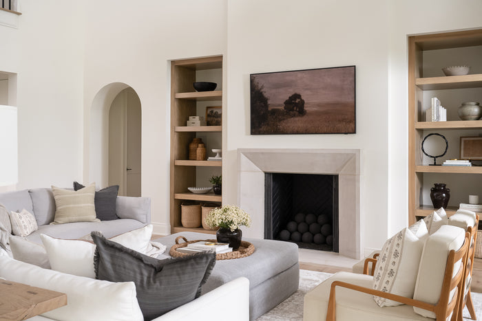 Round braided wicker tray or basket with two looped handles styled in a living room with cozy neutral tones. The natural fibers create a warm, rustic feel. | SW Home