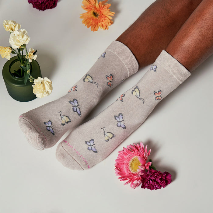 Light beige socks with butterfly patterns, paired with colorful flowers and a green vase on a white surface.