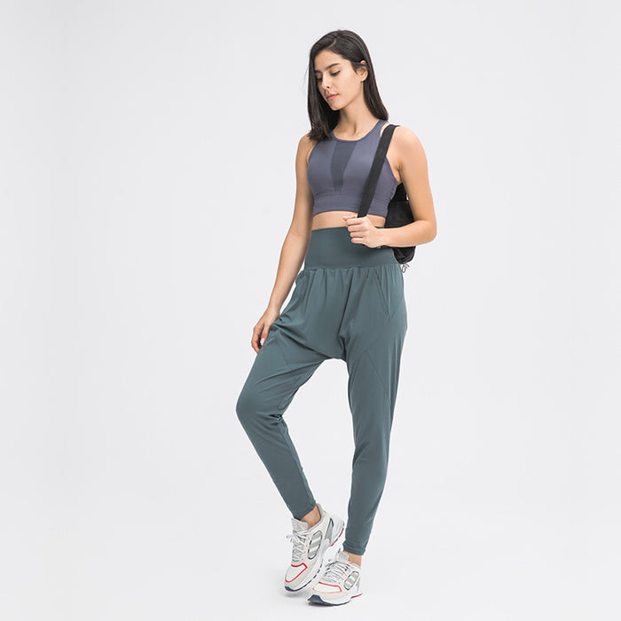 A woman standing, wearing casual stretch carrot pants in a moss green color, with a sports top and white sneakers.