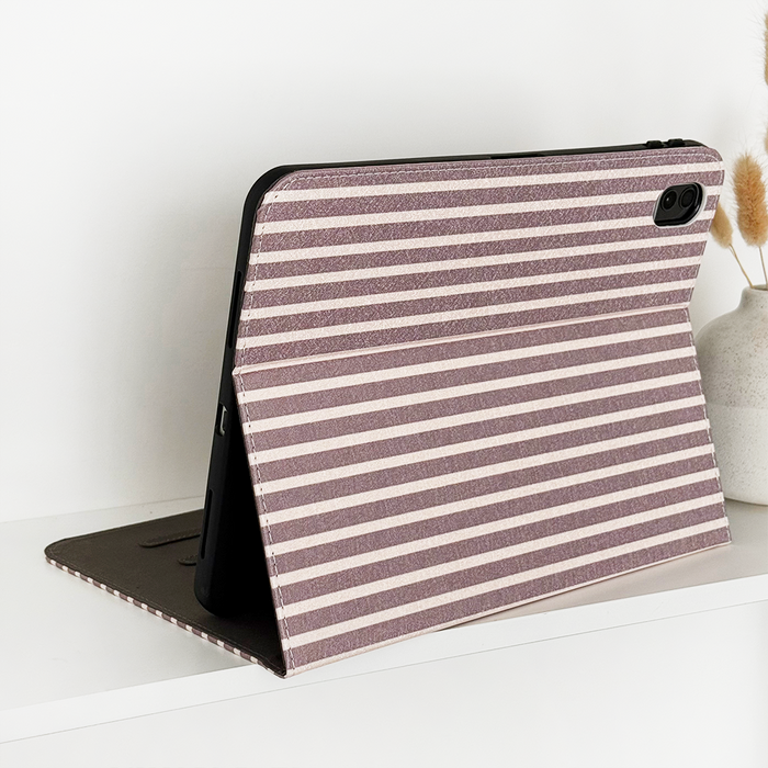 IPad in a Coconut Lane chestnut striped case on a white surface next to a vase of dried flowers.