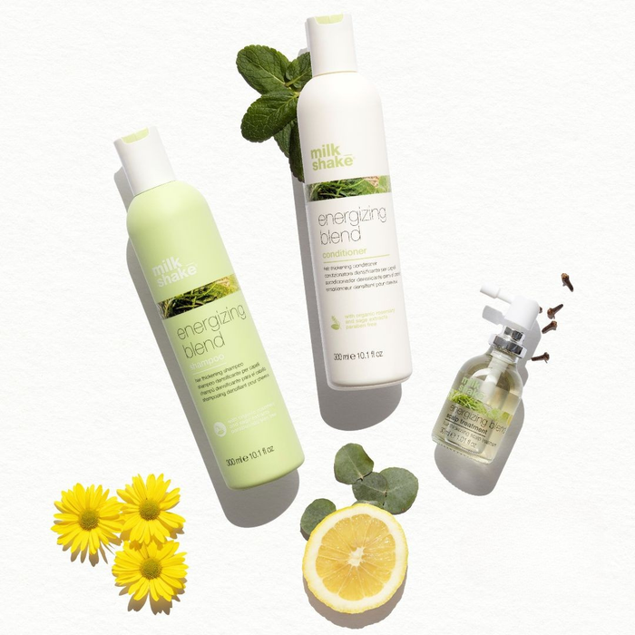 Three bottles of 'milk_shake' energizing blend with natural elements like flowers and a lemon on a white background.