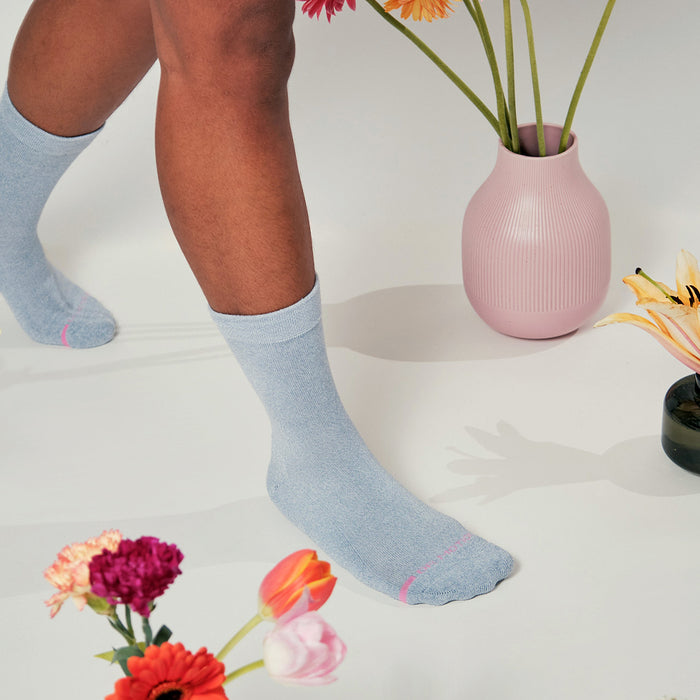 Light blue half cushion socks with pink accents, worn with flowers and vases in the background.