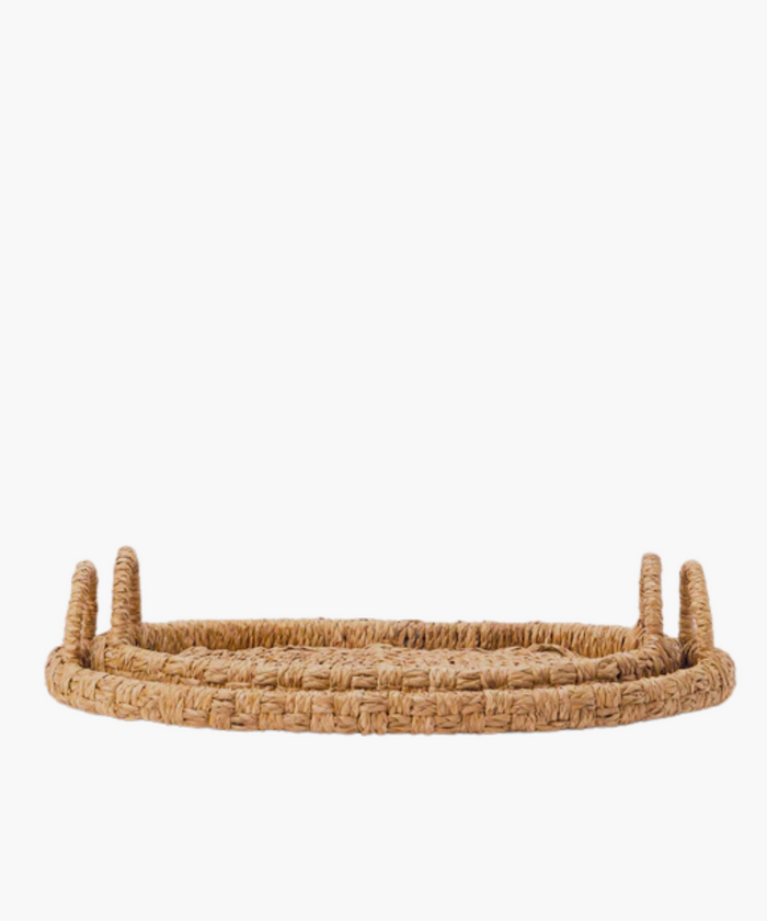 Oval hand-woven seagrass and rattan trays or baskets with two looped handles on each side in natural brown tones in two sizes. The tightly woven pattern suggests a sturdy, rustic style, suitable for home decor. | SW Home