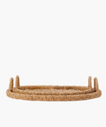 Oval hand-woven seagrass and rattan trays or baskets with two looped handles on each side in natural brown tones in two sizes. The tightly woven pattern suggests a sturdy, rustic style, suitable for home decor. | SW Home