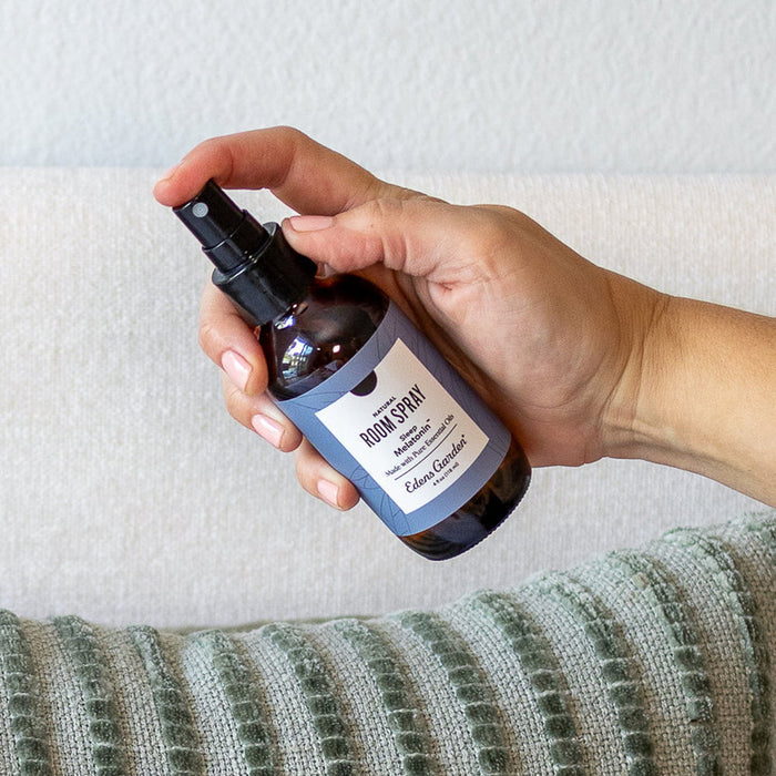 Hand holding a bottle of room spray with a label against a neutral background