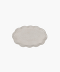 An oval, ceramic platter with a wavy, scalloped edge in a light cream color. The minimalist design conveys simplicity and elegance. | Wildwood Home Co.