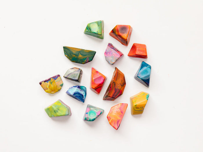 15 multi-colored rainbow rock crayons on a white background. Each crayon rock is shown in a variety of swirly hues that will color  with multiple colors when used on a paper.  Rocks are mini size and measure about 1-2" in length or width and 1/2" -1" in height. Size varies and the edges are very angular for crayons, making this a great gift for younger kids just learning to hold a crayon.