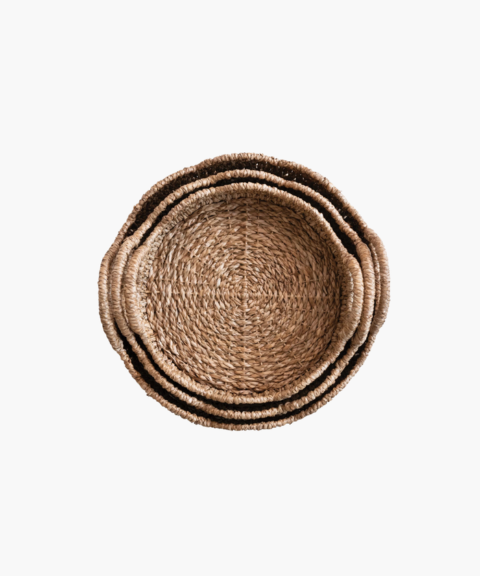 An overhead picture of three woven, round baskets with scalloped edges and two looped handles. Made of natural fibers, it evokes a rustic and earthy aesthetic. | SW Home