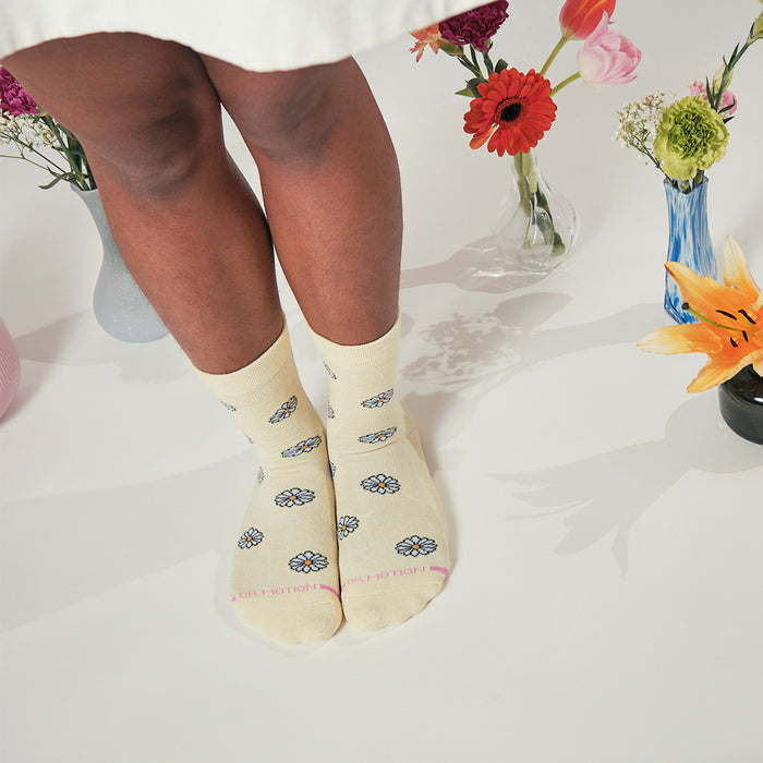 Yellow half cushion socks with blue daisy patterns, worn by a person standing among flower vases.
