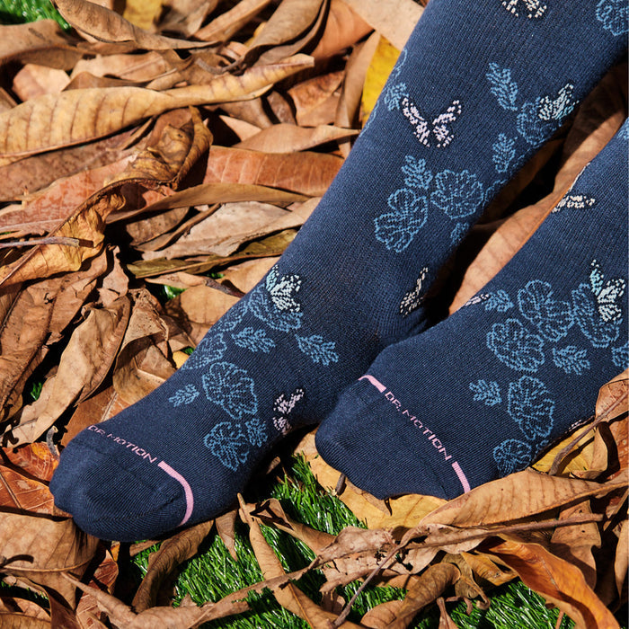 Knee-high compression socks with a navy background featuring whimsical butterfly and floral patterns.